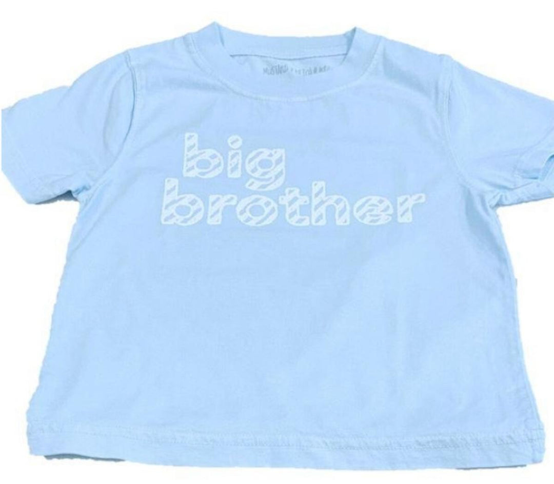 Mustard and Ketchup Kids pink and blue birthday t-shirts and big brother tee laid flat on a wooden surface, styled for a summer children's milestone gift guide at Cuddles and Carriages in Evans GA