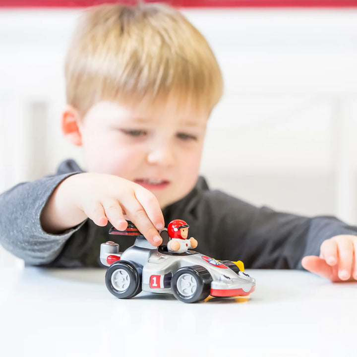 Child playing with a toy race car on a white surface
