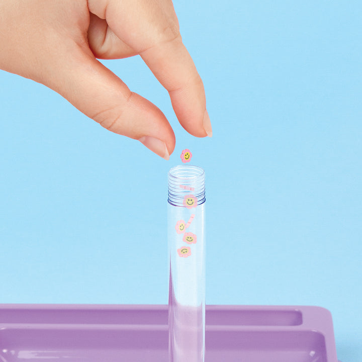 Hand placing small decorative items into a clear tube against a light blue background