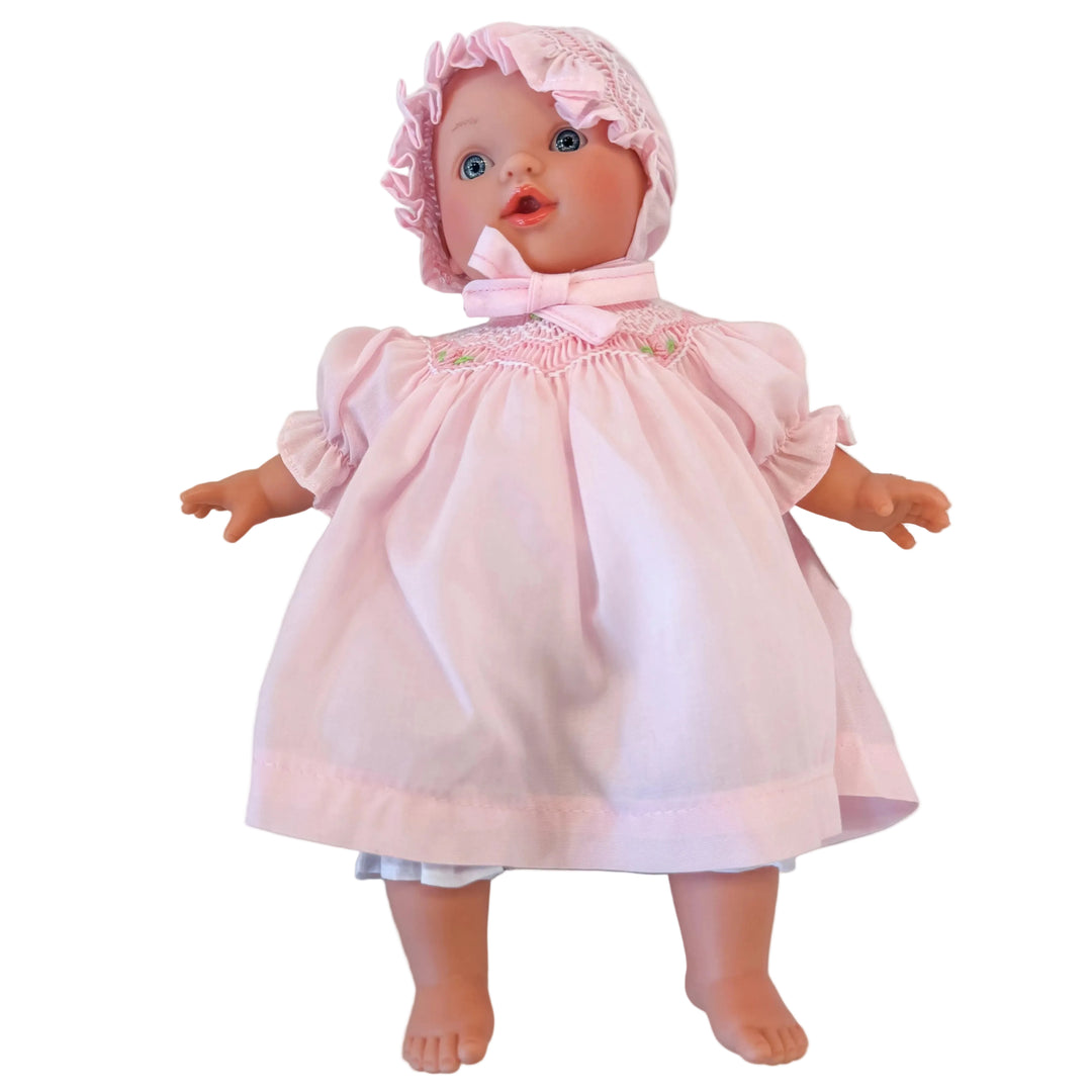 Baby doll wearing a pink dress and bonnet on a white background