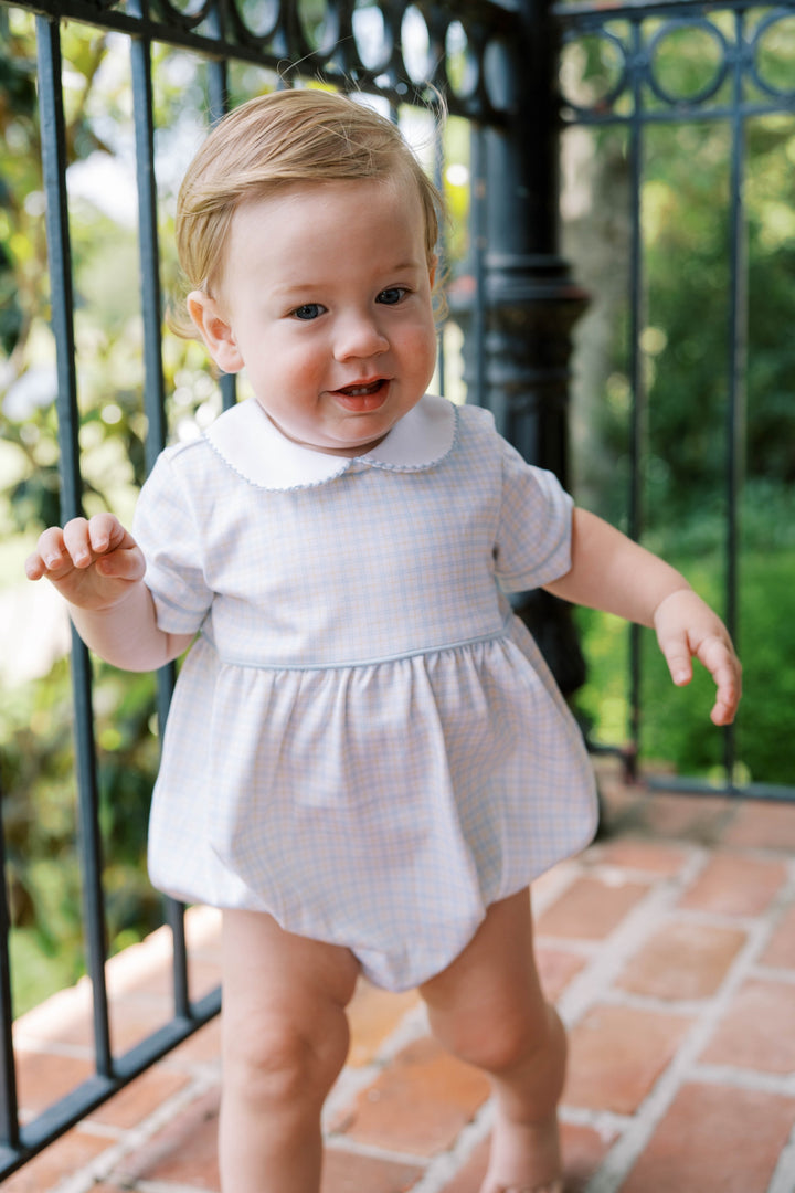 Babyboy in a light blue and yellow checked bubble standing outdoors on a brick patio.