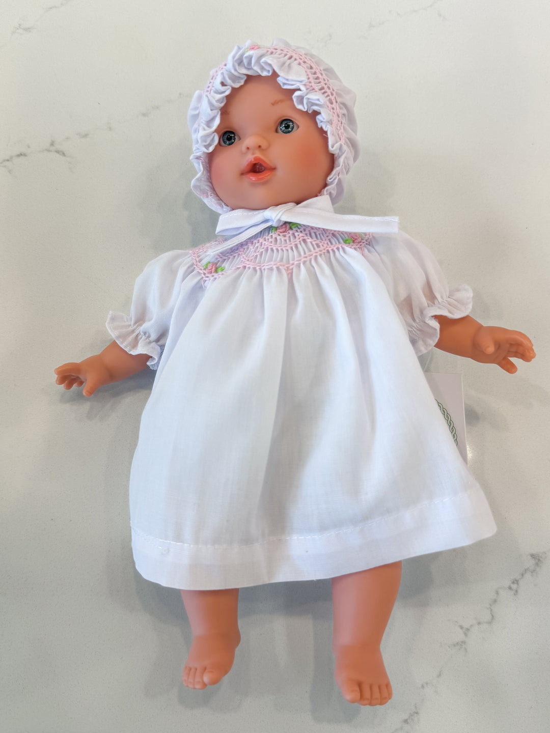 Doll wearing a white dress with lace trim and a matching bonnet on a light background