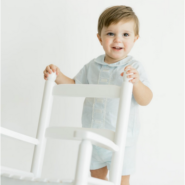 Child holding a white chair against a plain background