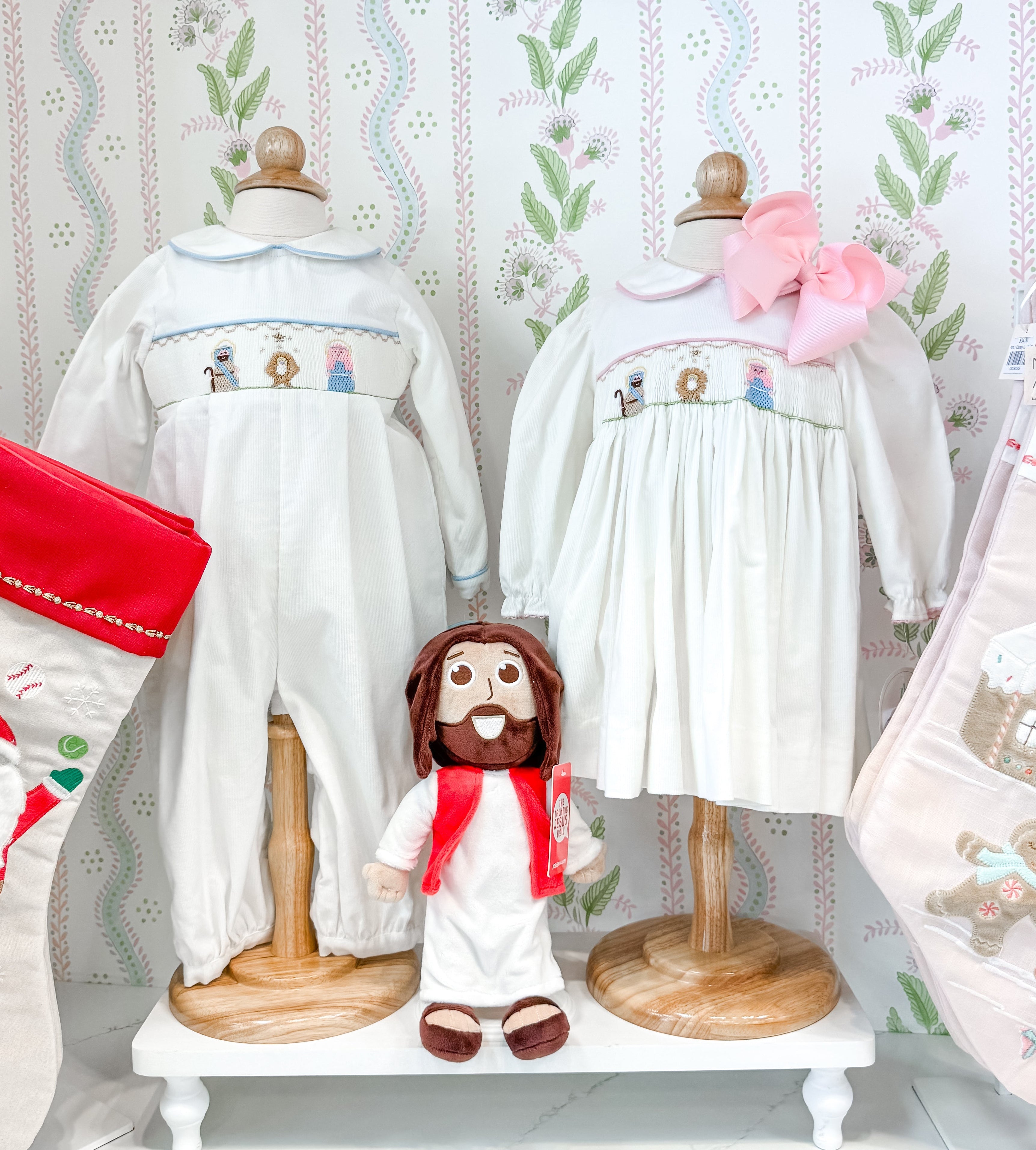 Display of embroidered clothing on mannequins against a decorative wallpaper background.