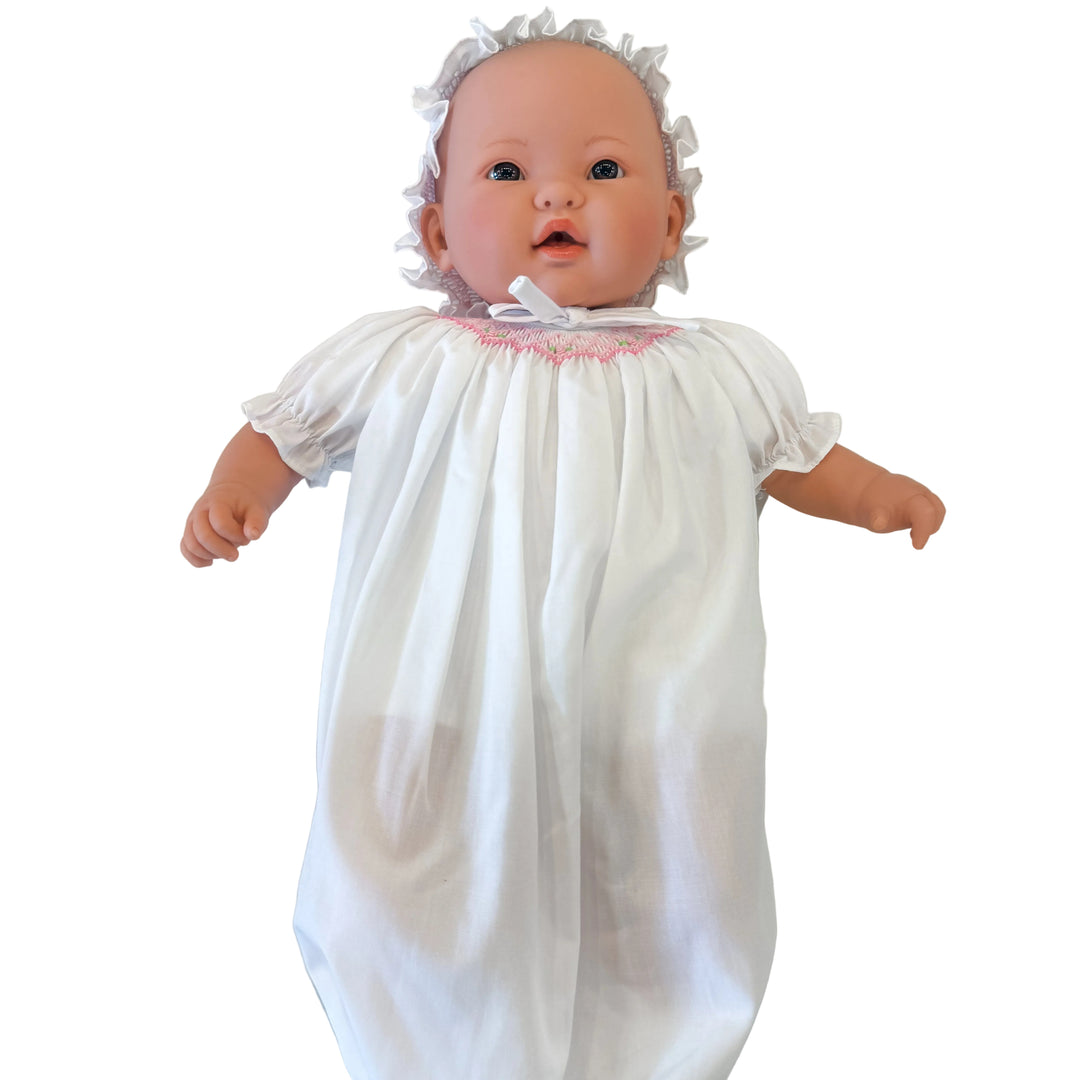Baby doll wearing a white dress with pink trim on a light gray background
