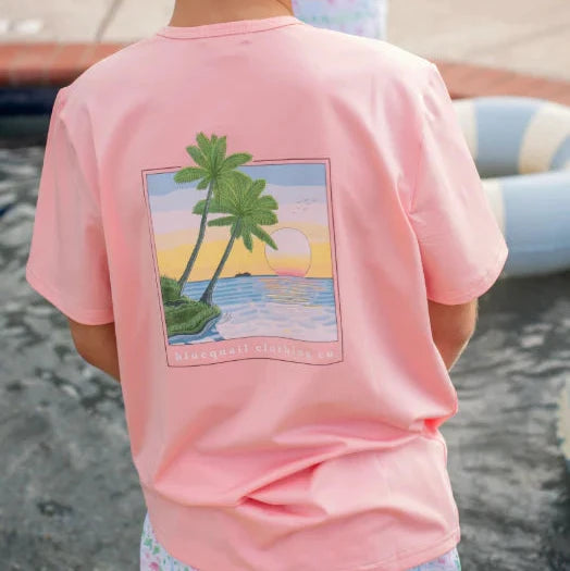 Child wearing a pink t-shirt with a palm tree design, standing by a poolside.