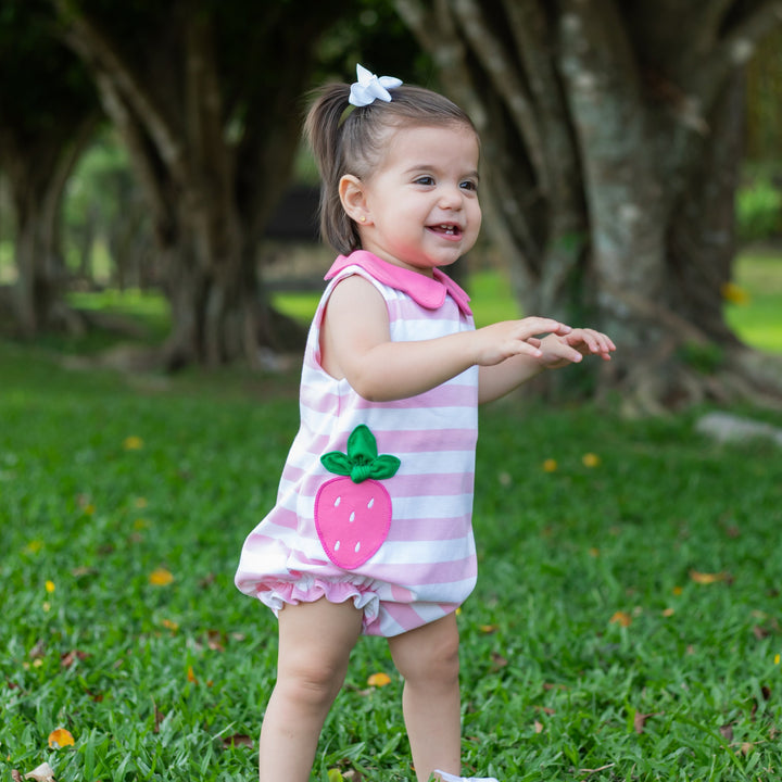 Child in a pink striped design with a strawberry design standing on grass